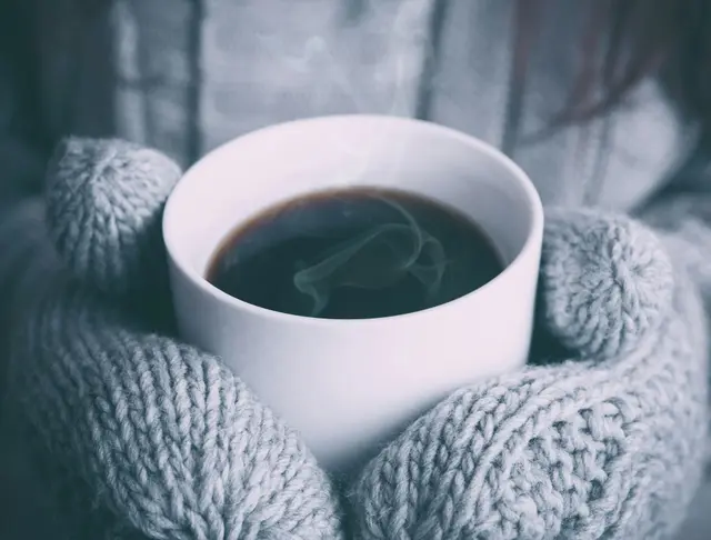 Manos con un pulóver tejido sosteniendo una taza caliente